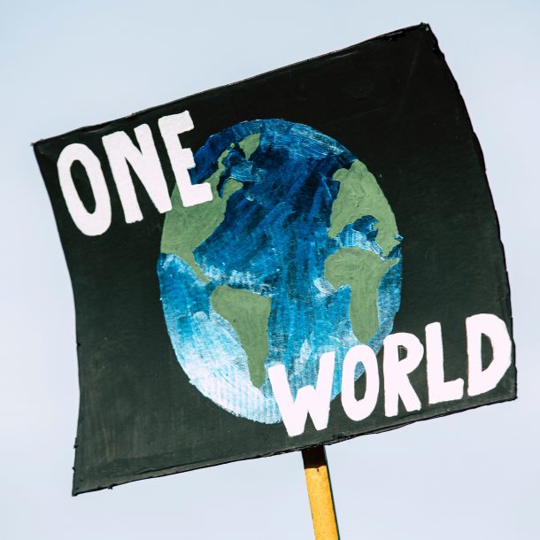 A black sign with the earth and the words "one world" on it at a climate rally. Protestors encourage corporations to make their businesses more sustainable.