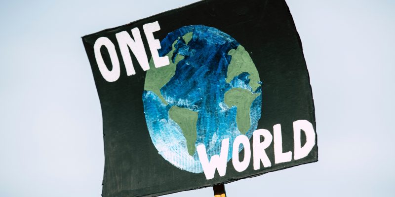 A black sign with the earth and the words "one world" on it at a climate rally. Protestors encourage corporations to make their businesses more sustainable.