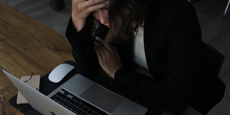A woman sitting at a desk in front of a laptop with her head in her hands. It accompanies an article about hustle culture.