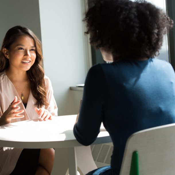 Two people sitting at a round table. One has long brown hair and is facing the viewer, and the other has an afro and is facing away from the viewer. The photo accompanies an article about business coaching.